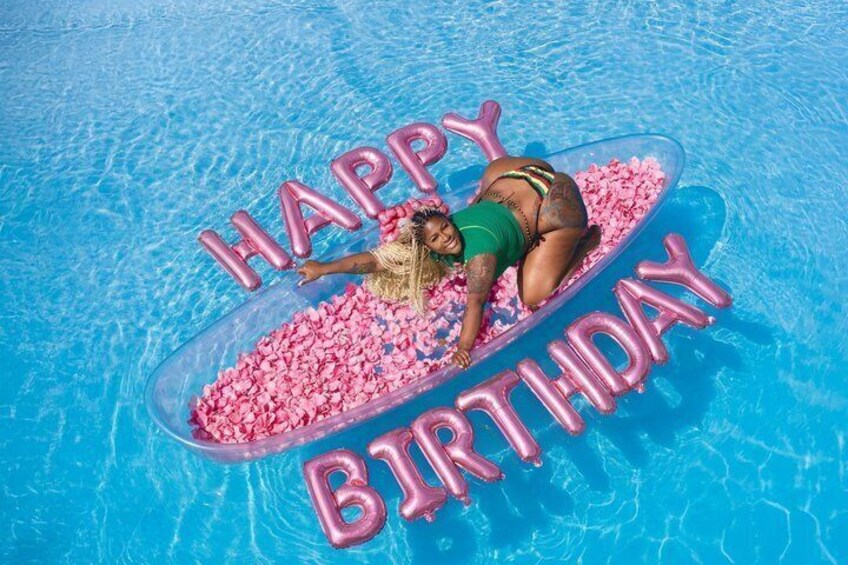 A person lying on a floating platform in a pool with pink balloons spelling 'HAPPY BIRTHDAY'. 2