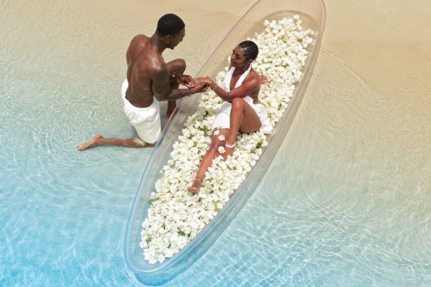 A couple in a transparent tub filled with white flowers, sitting in a pool. 2
