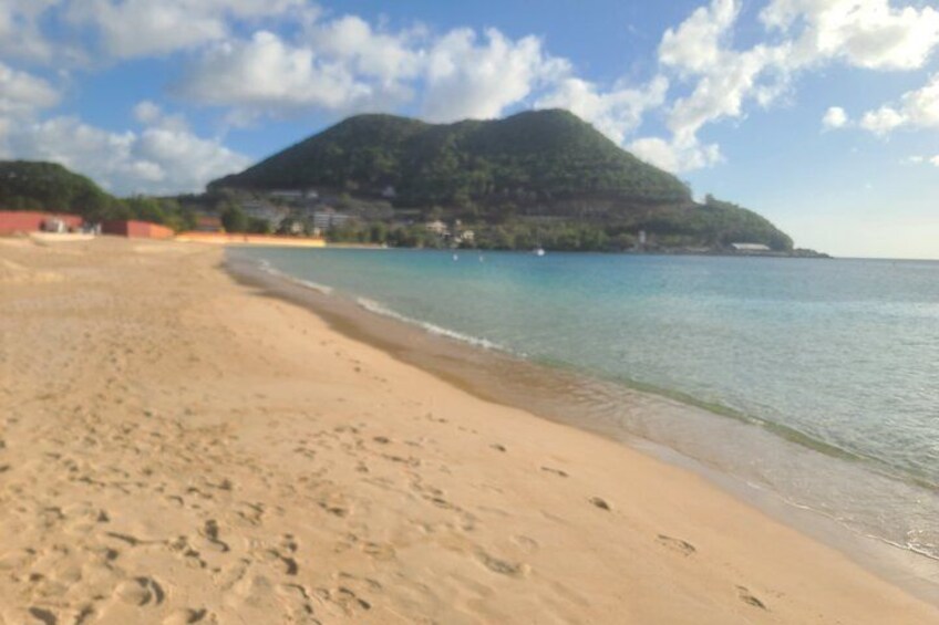 A sandy beach with footprints, calm water, and a mountain in the background. 3