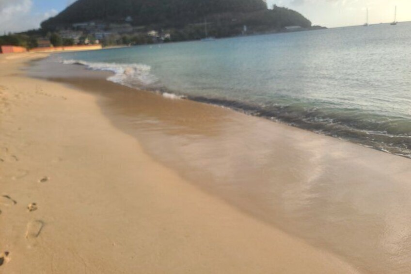 A sandy beach with gentle waves, a clear sky, and a distant mountain. 5