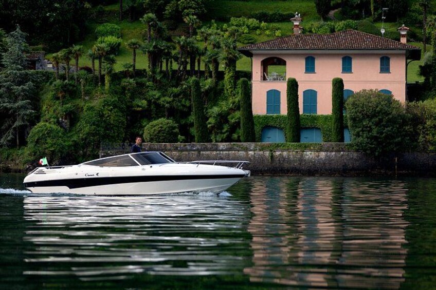 A white motorboat on calm water, a pink house with green shutters, and a well-maintained garden with tall trees. 5