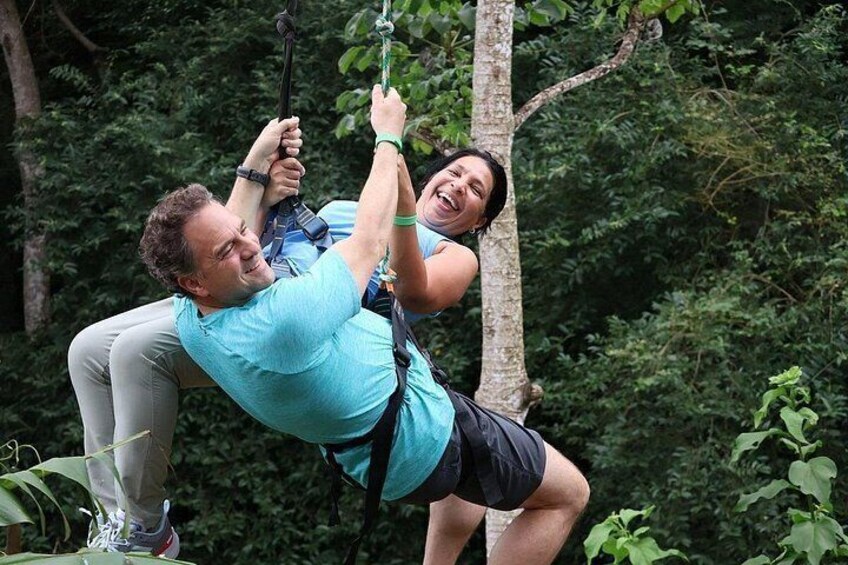 Två personer åker på en zipline genom en skog. 2