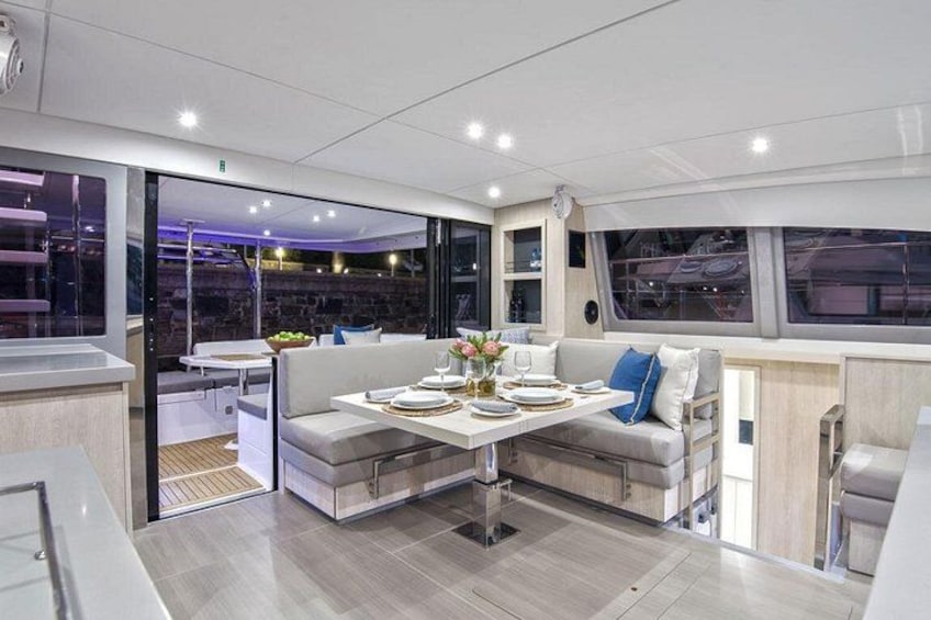 A modern yacht interior with a dining area, a sofa, and a table set for a meal. 3