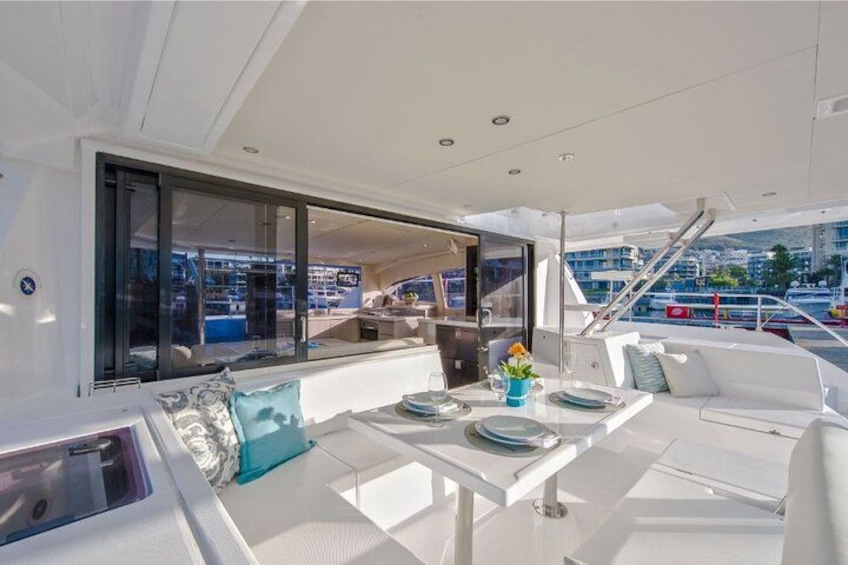 A yacht's deck with a dining table, white cushions, and a view of the marina. 2