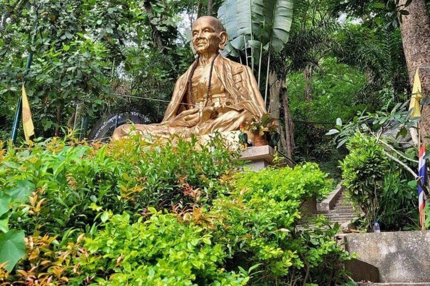 Een gouden standbeeld van een zittende figuur in een weelderige tuin. 2