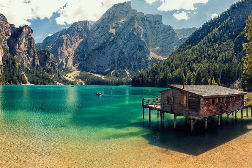 Una cabaña de madera sobre pilotes junto a un lago turquesa, con montañas al fondo. 2