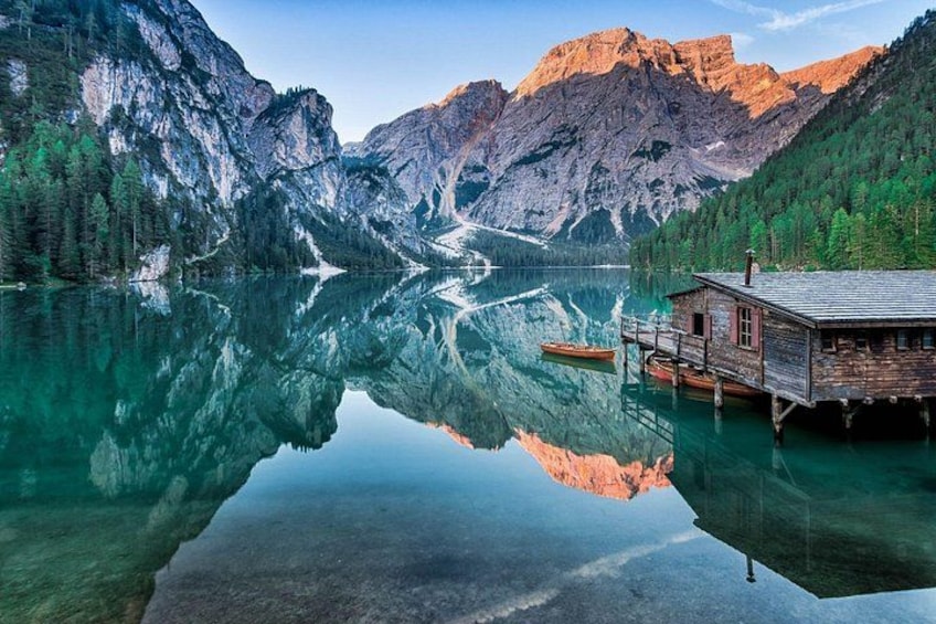 Un lago tranquillo con una baita di legno e un molo, circondato da montagne e una fitta foresta. 4
