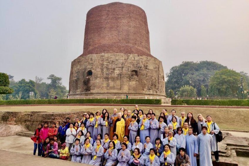 A group of people posing in front of a large brick structure with a dome, surrounded by greenery. 1