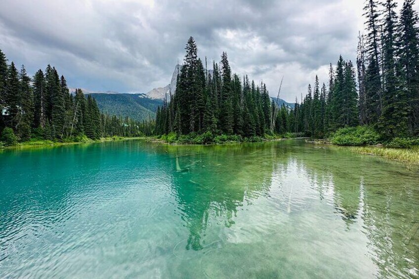 A clear turquoise lake surrounded by dense evergreen forest and mountains in the background. 2