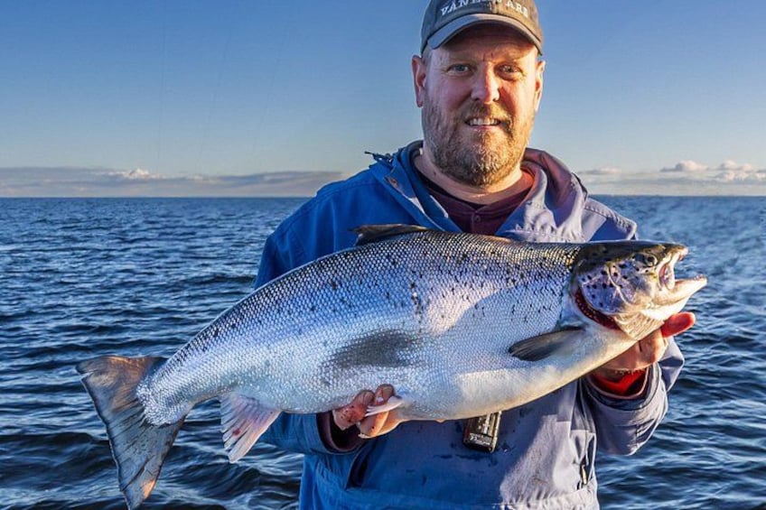 A person holding a large fish in a body of water with a clear sky in the background. 4