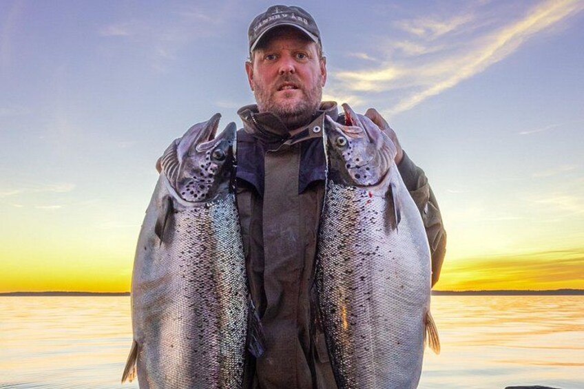 A person holding two large fish against a sunset backdrop. 3