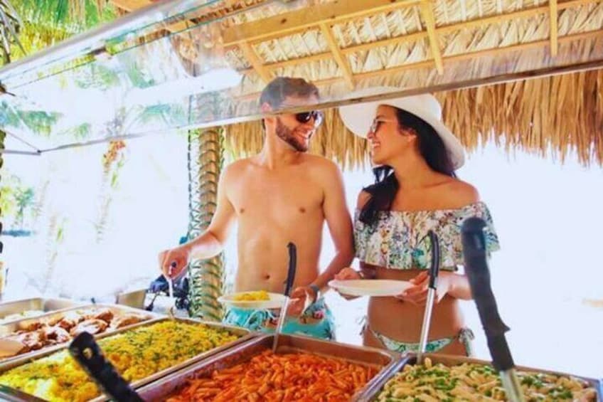 Un buffet proposant une variété de plats, un toit de chaume et des palmiers en arrière-plan. 1