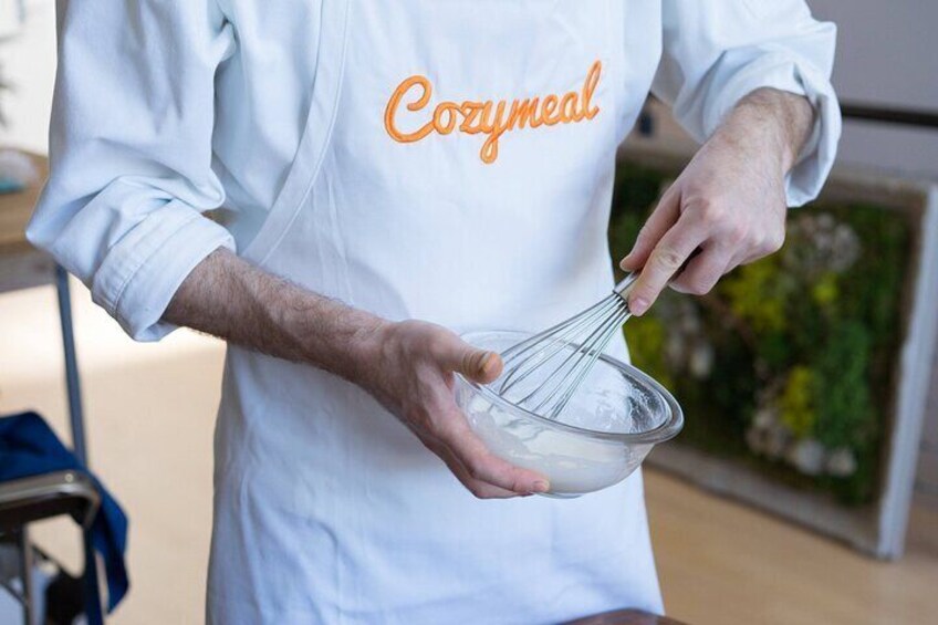 A person wearing a white apron with the word "Cozymel" on it, holding a whisk. 5