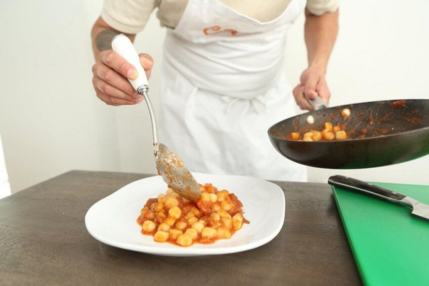 Una persona con delantal blanco sirve garbanzos de una sartén a un plato blanco. 2