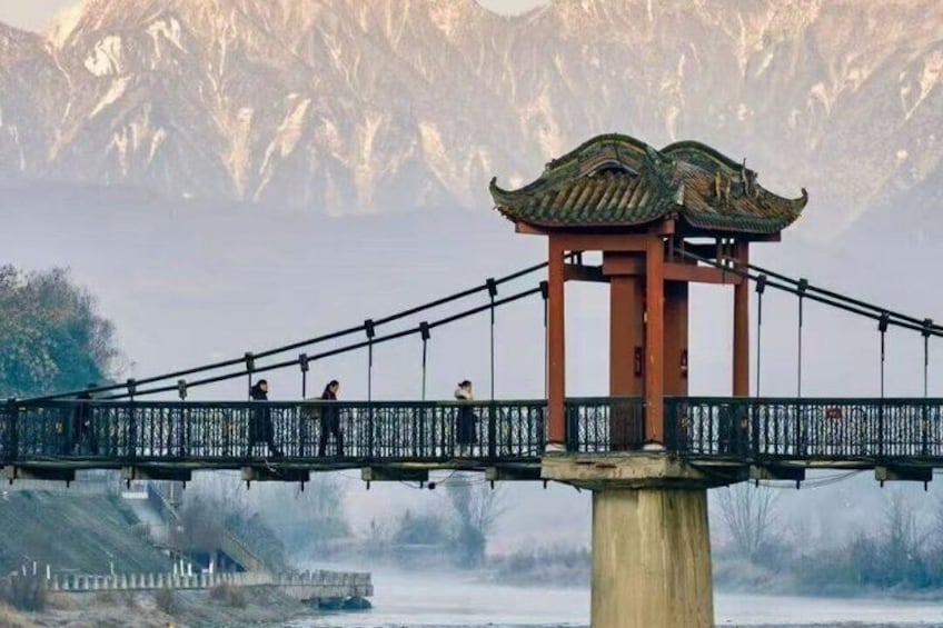 Un pabellón chino tradicional sobre un puente, cruzando un río, con montañas al fondo. 1