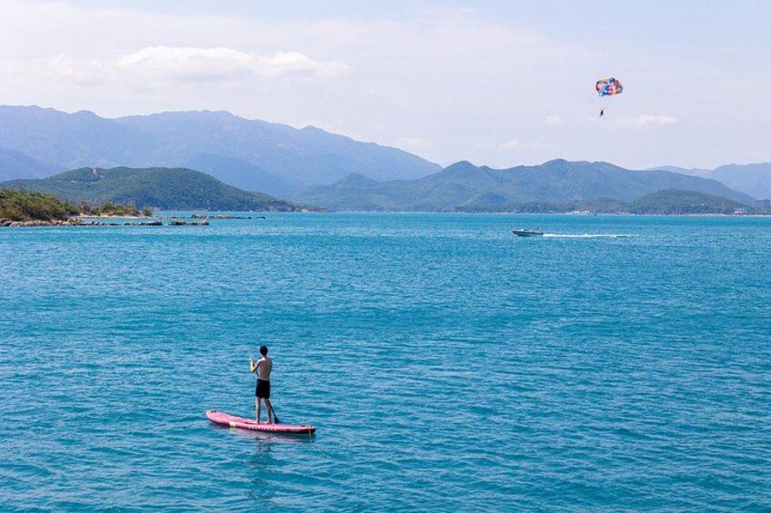 A person paddleboarding on a calm sea with mountains in the background. 3