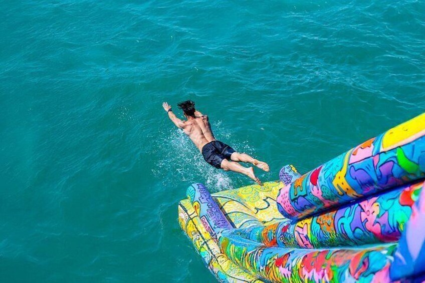 A person swimming in clear blue water, a colorful inflatable surfboard, and a vibrant mural. 3