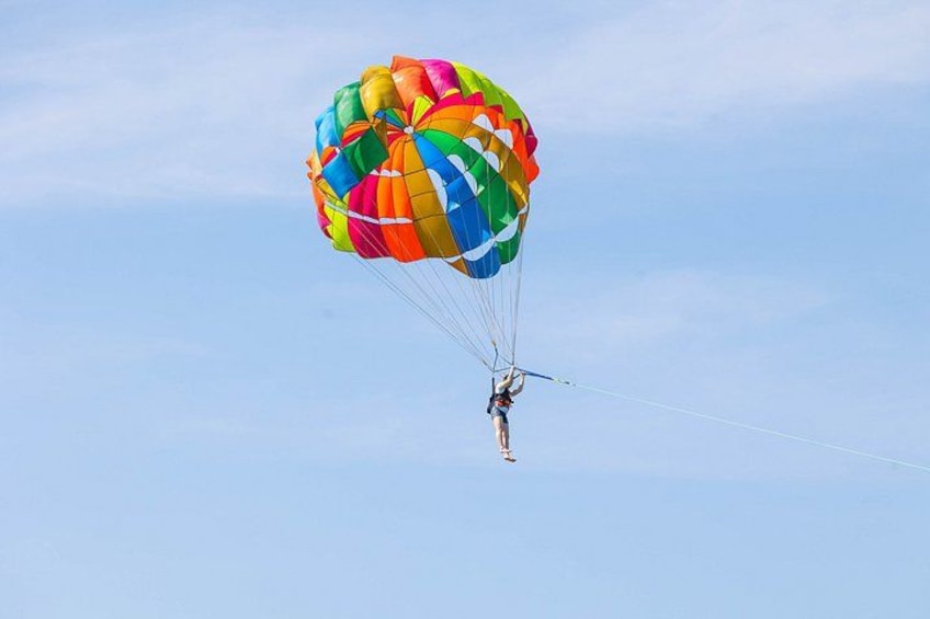 Eine Person mit bunten Fallschirm beim Fallschirmspringen vor blauem Himmel. 3