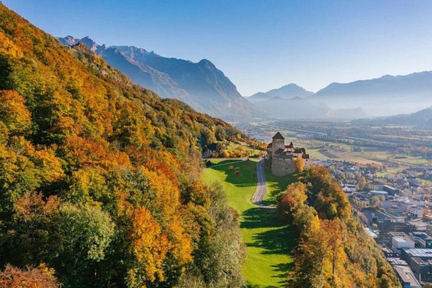 Un château perché sur une colline, entouré d’un paysage automnal aux couleurs flamboyantes, une route sinueuse et une vallée en contrebas. 5