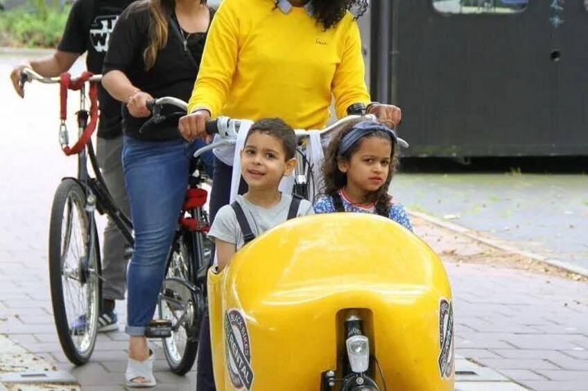 A woman and two children on bicycles, a yellow scooter, and a red bicycle in an outdoor setting. 5
