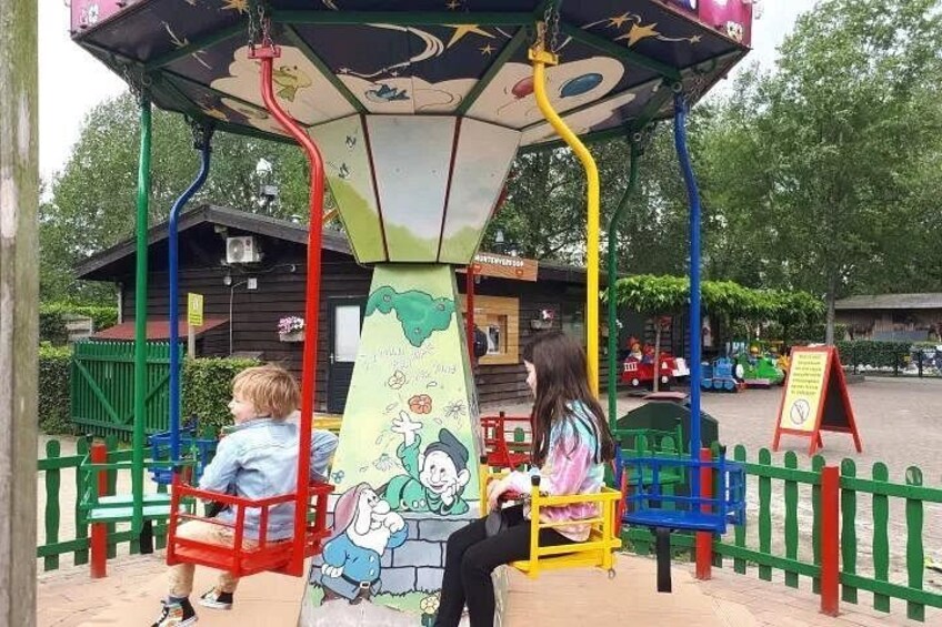 Two children on swings at a playground with a colorful mural on the central structure. 4