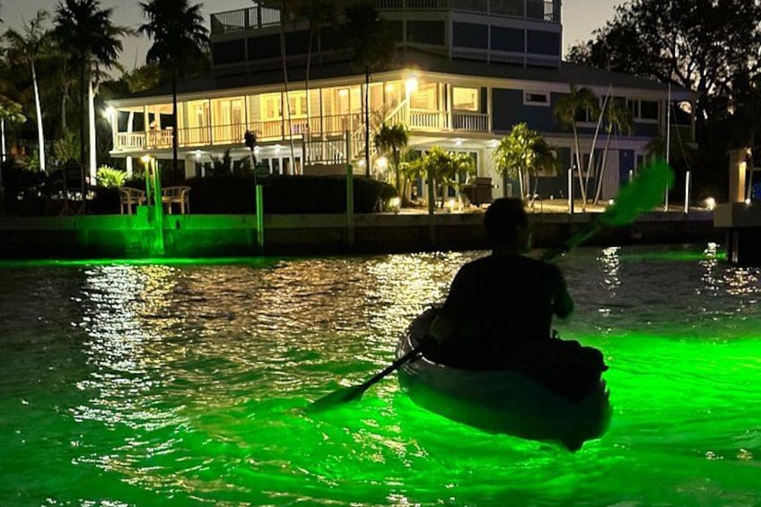 Una persona practica kayak en un cuerpo de agua con iluminación verde nocturna. 1