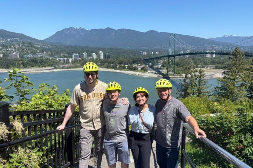 A group of people wearing helmets, standing on a bridge with a view of a river and mountains in the background. 5