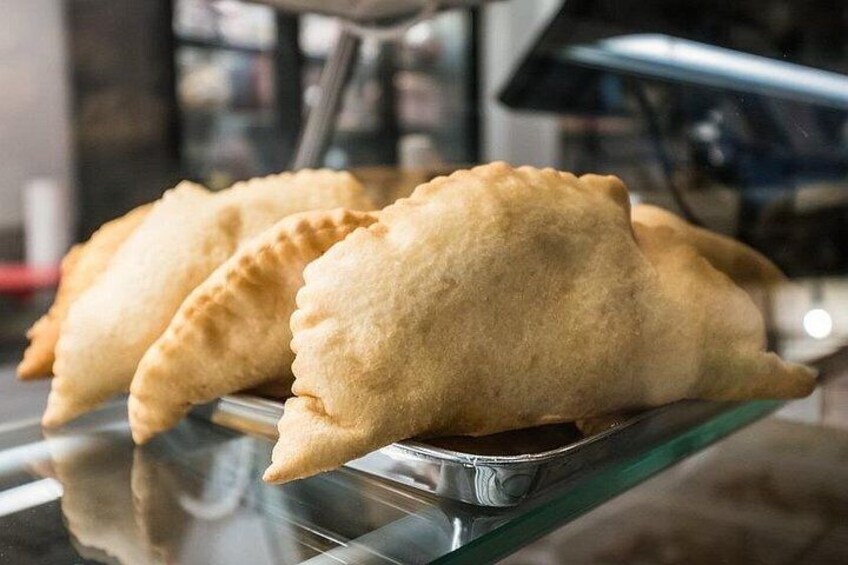 Three golden-brown empanadas on a glass display. 5