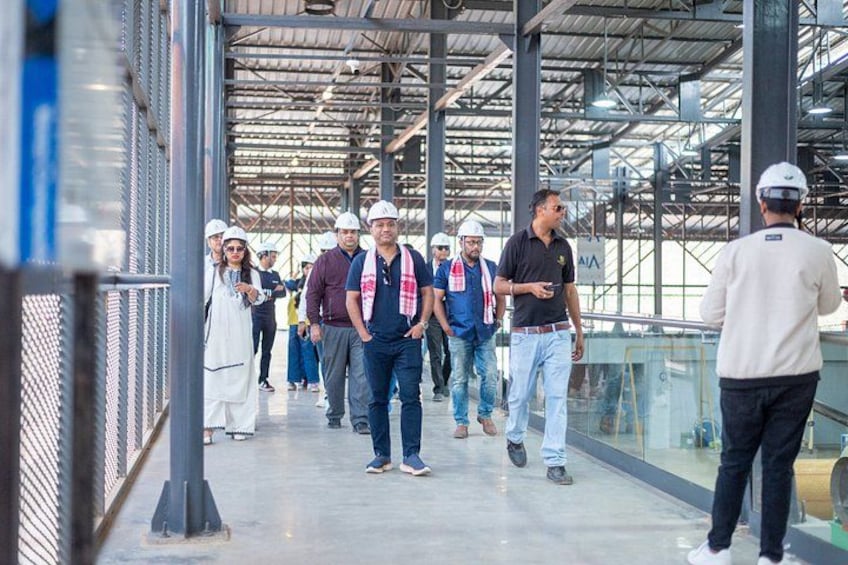 A group of people walking in an industrial area with metal structures and a glass walkway. 2