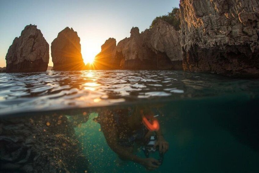 A diver underwater with a sunlit rock formation in the background. 4