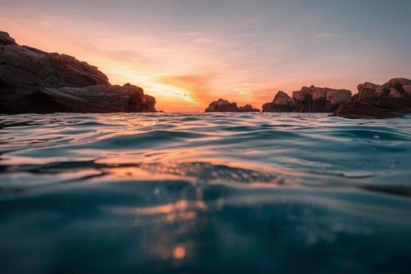 A sunset over a rocky coastline with waves in the foreground. 3