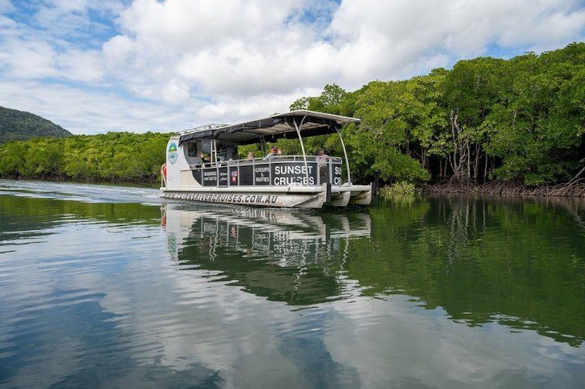 Een boot genaamd 'Sunset Cruises' op kalm water, met weelderige begroeiing op de achtergrond. 3