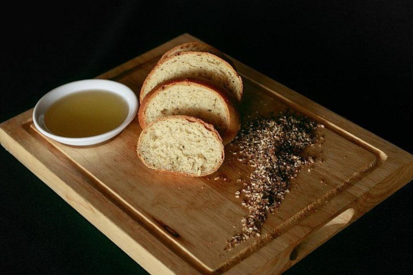 Sliced bread on a wooden board with a bowl of olive oil and scattered herbs. 2