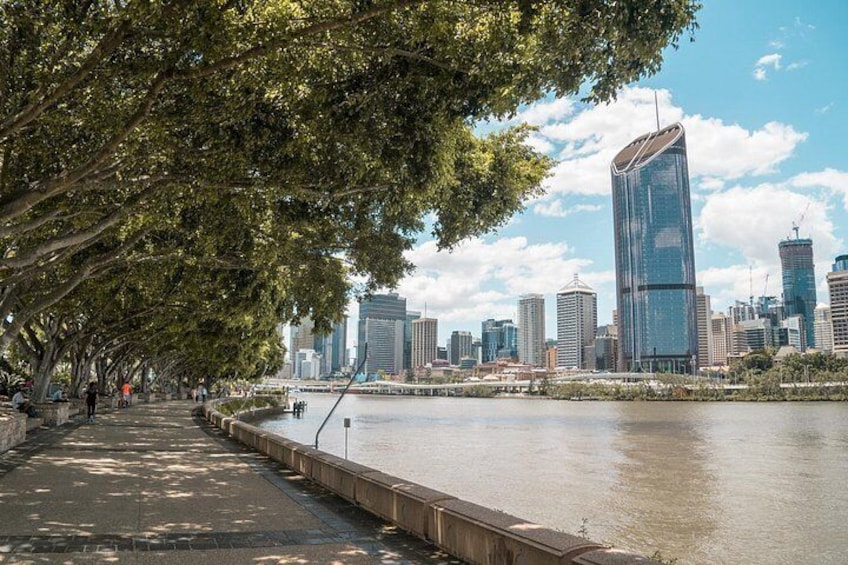 A riverside walkway lined with trees, a modern city skyline, and a prominent skyscraper. 5