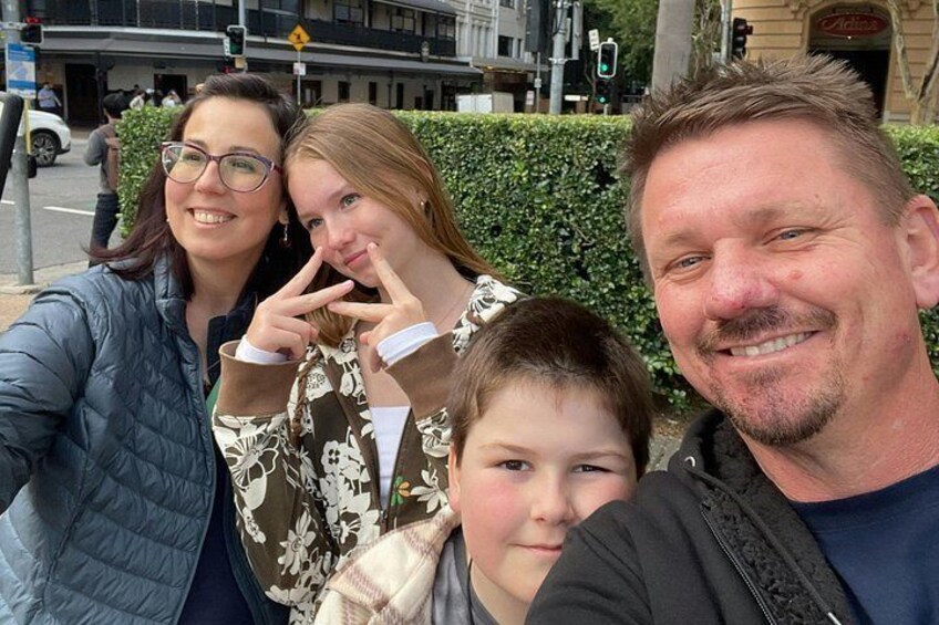 A group of people posing for a selfie on a city street with buildings and traffic lights in the background. 2