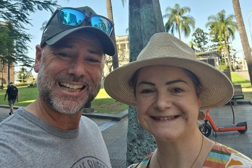 A man and a woman in a park with palm trees and a building in the background. 4