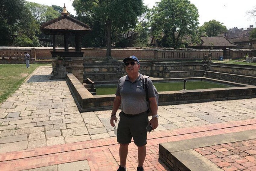 A man standing in a park with a pond and a gazebo in the background. 2