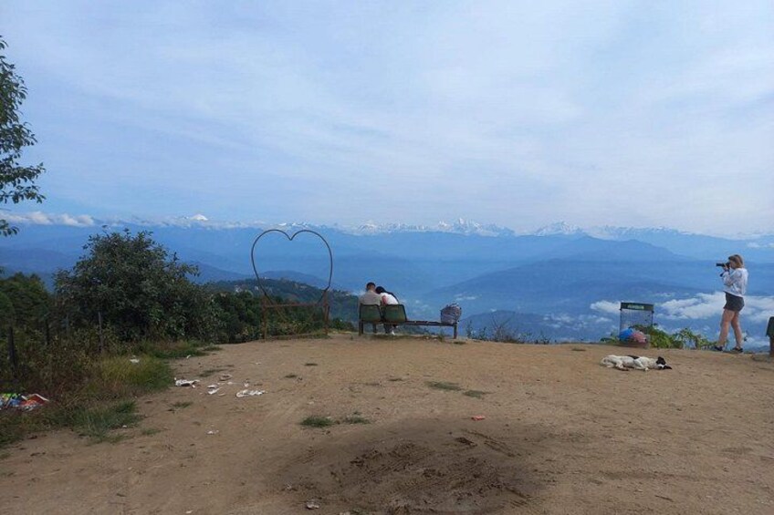 A dirt path with a heart-shaped structure, a person sitting on a bench, and another person taking a photo. 5