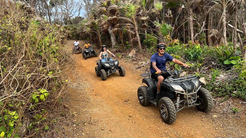 A group of people riding ATVs on a dirt path surrounded by dense vegetation. 2