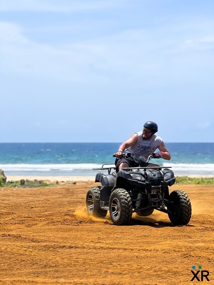 A person riding an ATV on a dirt path near the ocean. 5