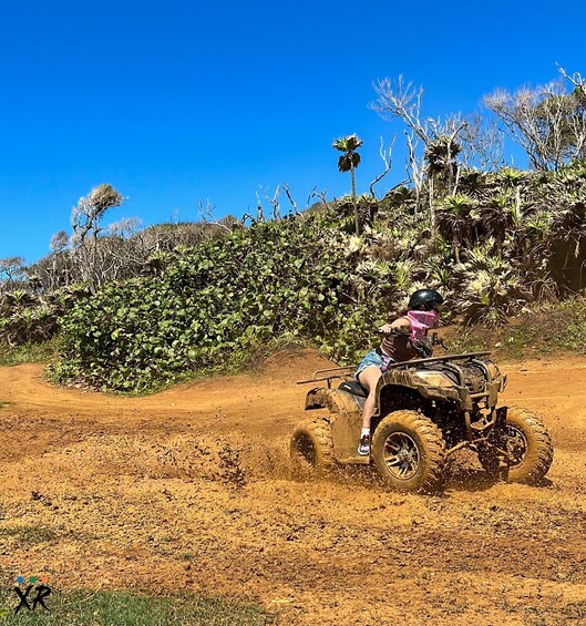 A person riding an ATV on a dirt path surrounded by vegetation. 3