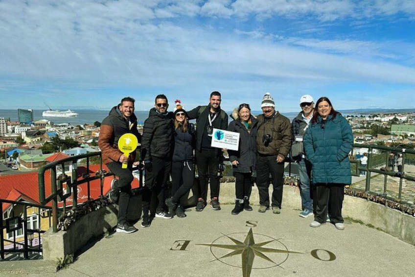 A group of people standing on a concrete platform with a compass design, overlooking a cityscape with buildings and a body of water. 2