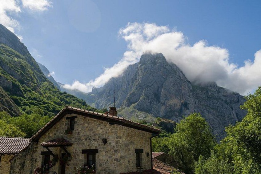 A stone building with a tiled roof, surrounded by lush greenery and mountains in the background. 5