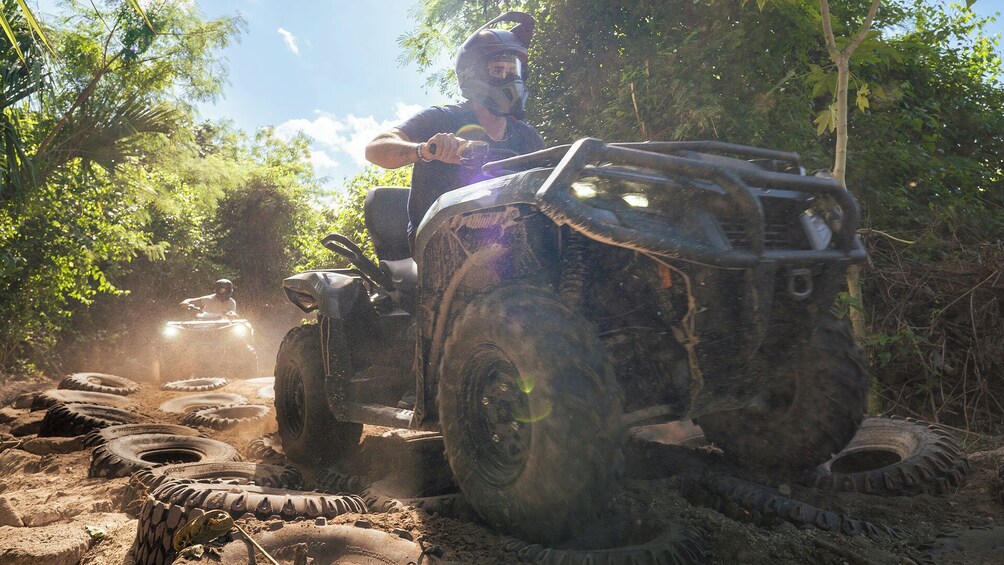 Una persona conduciendo un cuatrimoto por un camino de tierra rodeado de árboles. 1