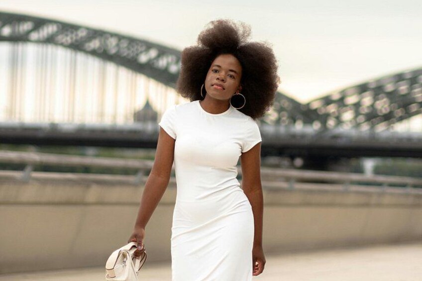 A person in a white dress walking with a pair of shoes in hand, with a bridge in the background. 3