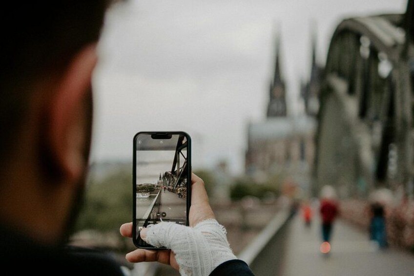 A person holding a smartphone, capturing a bridge with a cityscape in the background. 2