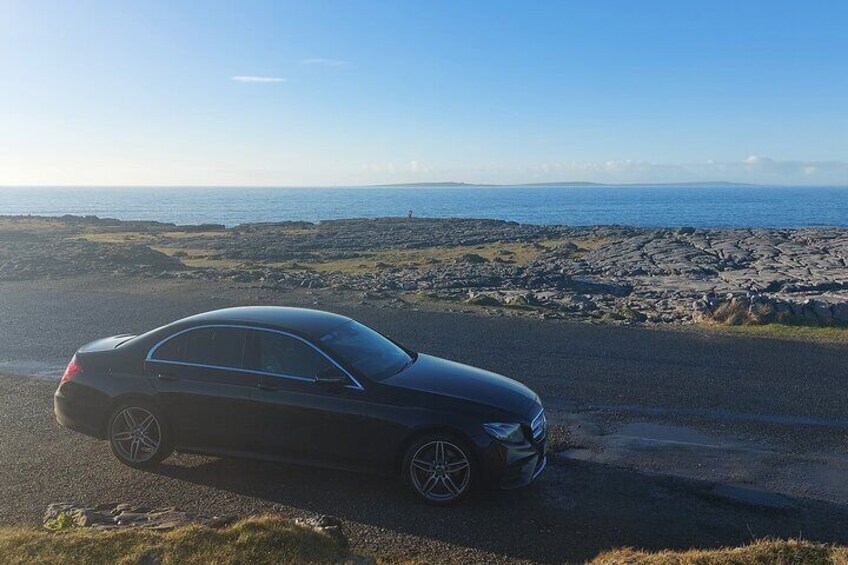 Un coche negro estacionado en una carretera costera con un paisaje rocoso y el mar al fondo. 5