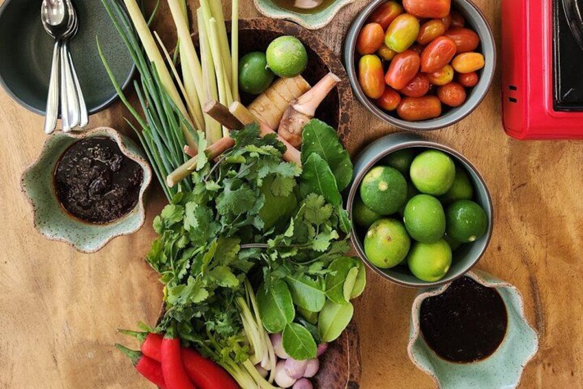 A wooden table with various ingredients including limes, cilantro, green onions, and chili peppers. 2
