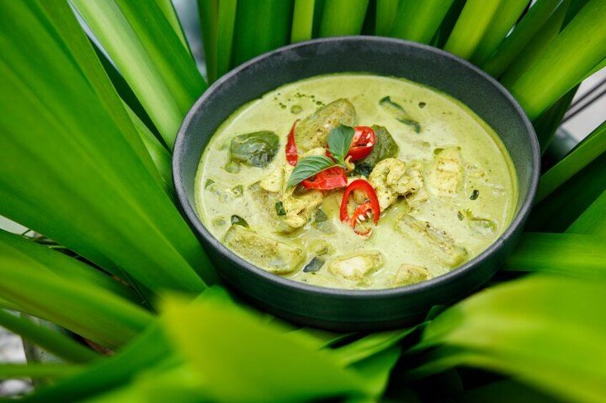 A bowl of green curry with red chili slices and basil leaves on a black plate. 3