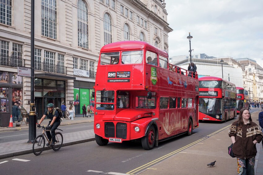 A red double-decker bus labeled 'RM1' on a city street with pedestrians and a cyclist. 2